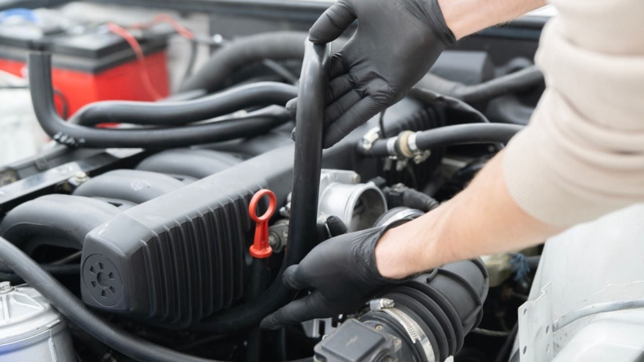 Mechanic works on installing air hose inside the engine compartment of a vehicle, ensuring proper function at an auto repair shop.