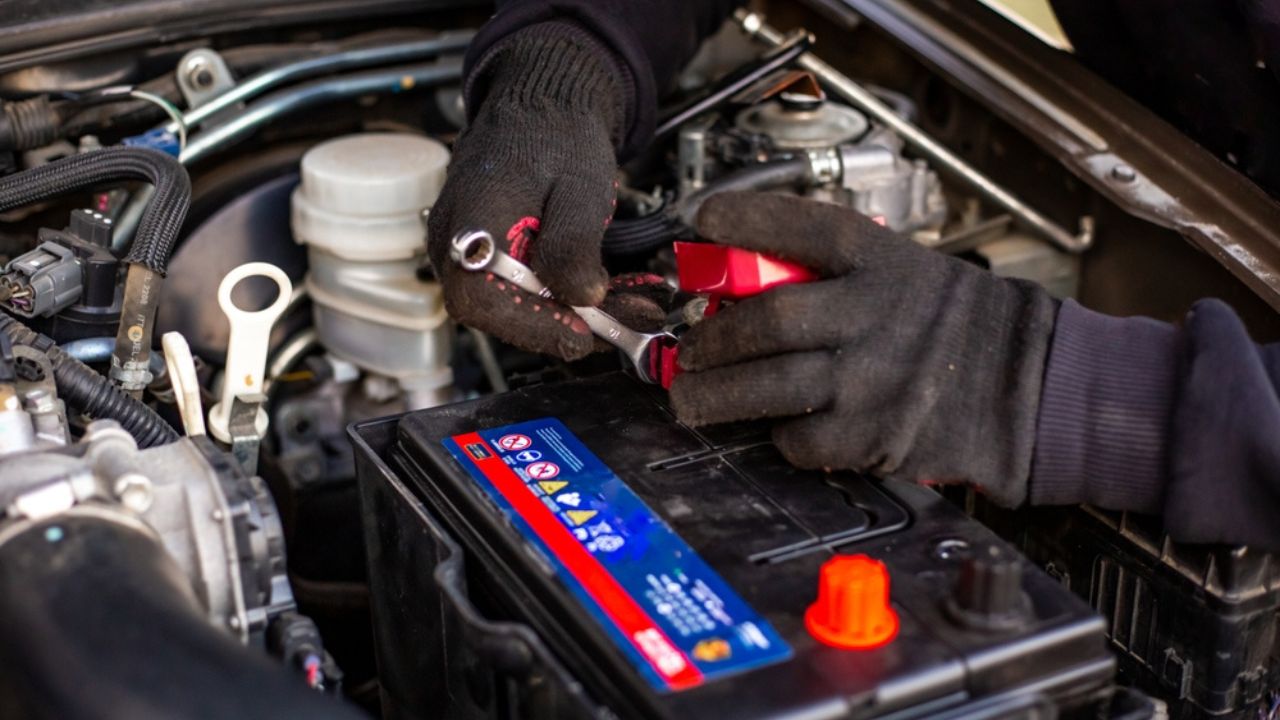 Replacing a car battery. A man installs a battery by tightening the terminals with a wrench under the hood of a car.