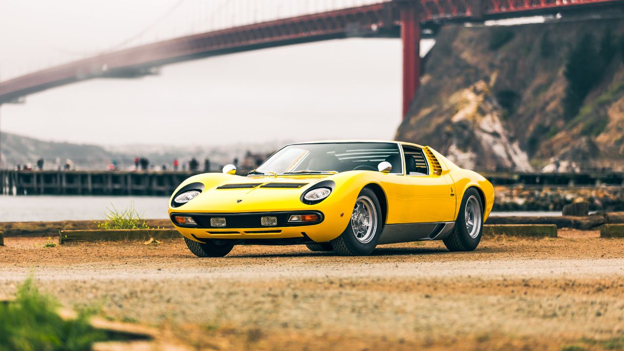 San Francisco, CA, USA Yellow Lamborghini Miura parked in a gravel lot with the Golden Gate Bridge and fog in the background