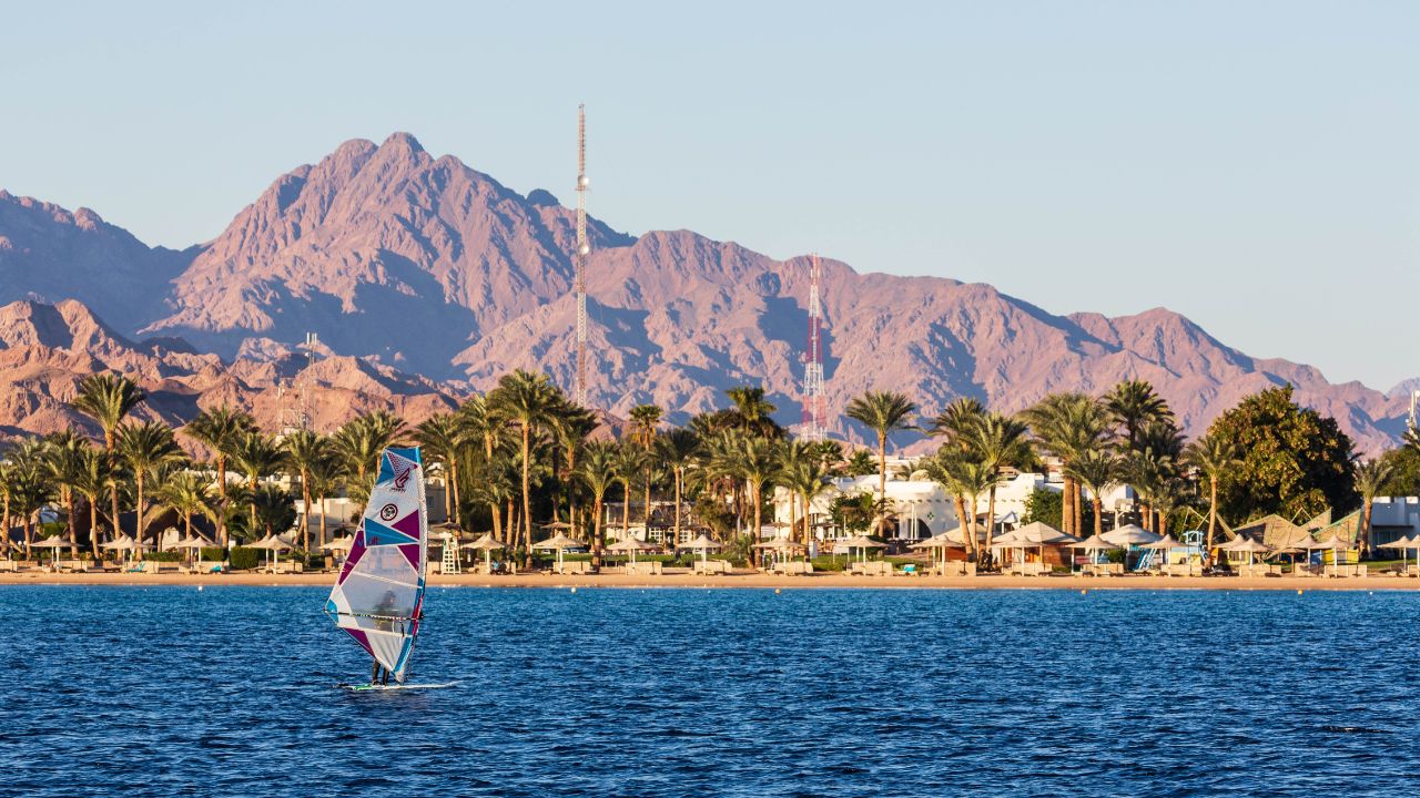 Dahab, Egypt - January 2022: Windsurfing sail in Lagoon beach on the Red Sea with blue water against the coast with white buildings, palm trees and mountains