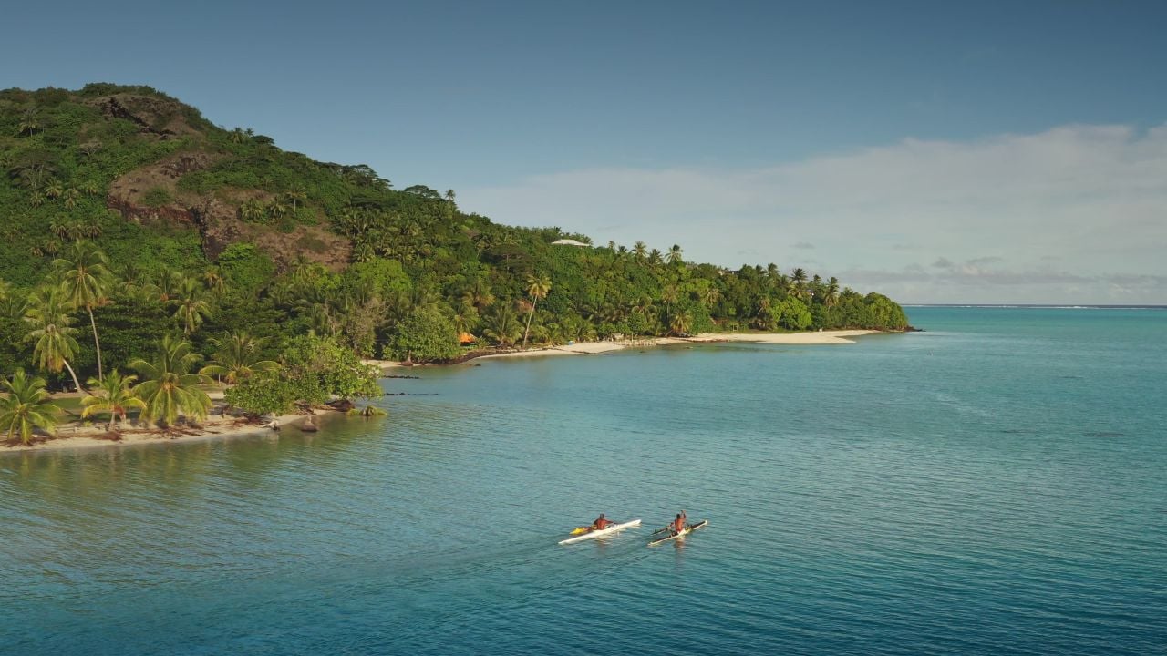 Two tourists kayaking near white sand beach in Maupiti, French Polynesia, surrounded by lush vegetation and crystal clear waters. Wild travel destination, remote nature paradise, active outdoor sport
