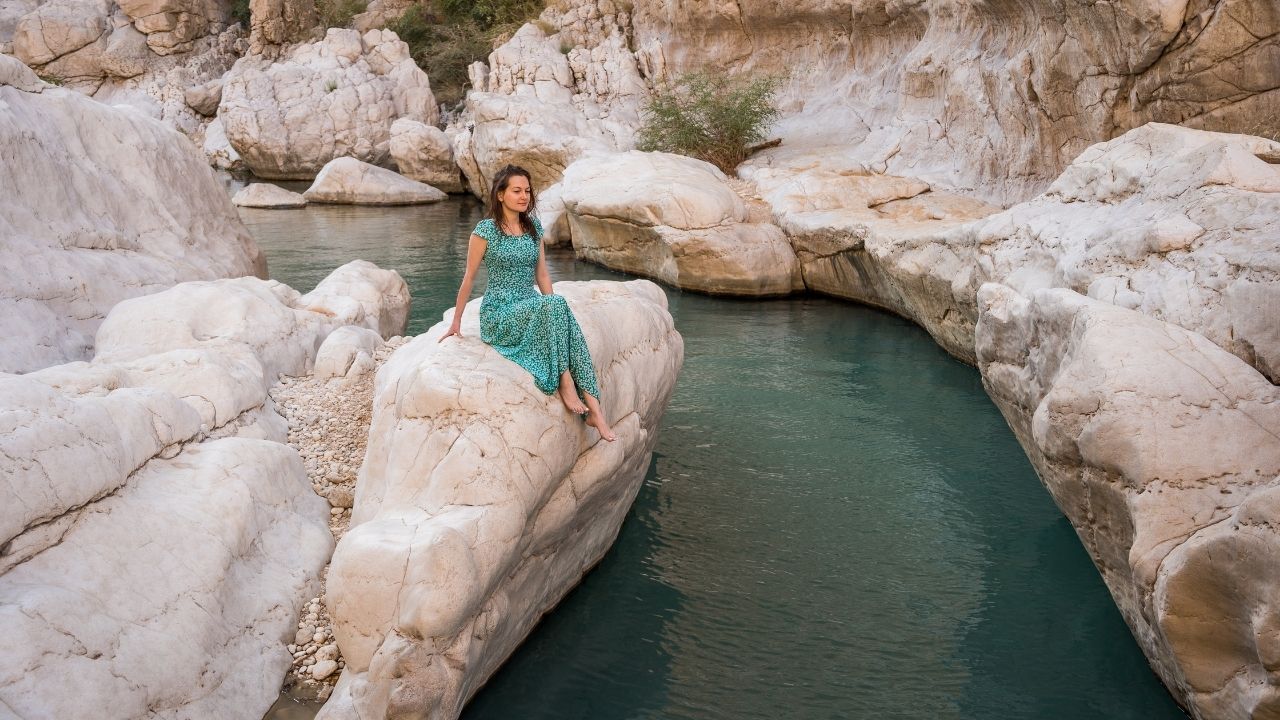 Woman in turquoise dress sitting near Wadi Bani Khalid pool