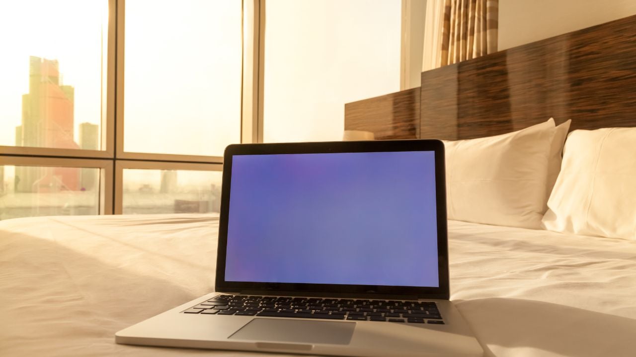 Laptop computer on white bed sheets in cozy hotel room with copy space blank screen