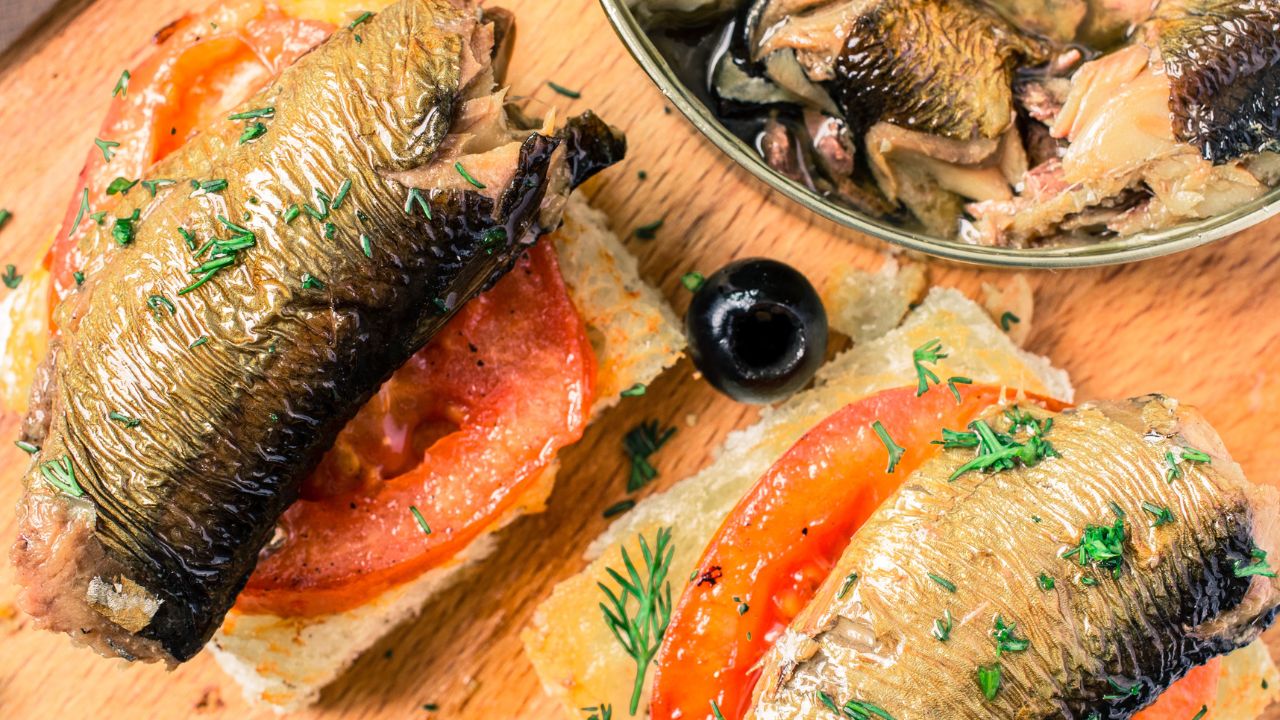 Toasts with a large smoked sardines. On the table hot peppers and olives