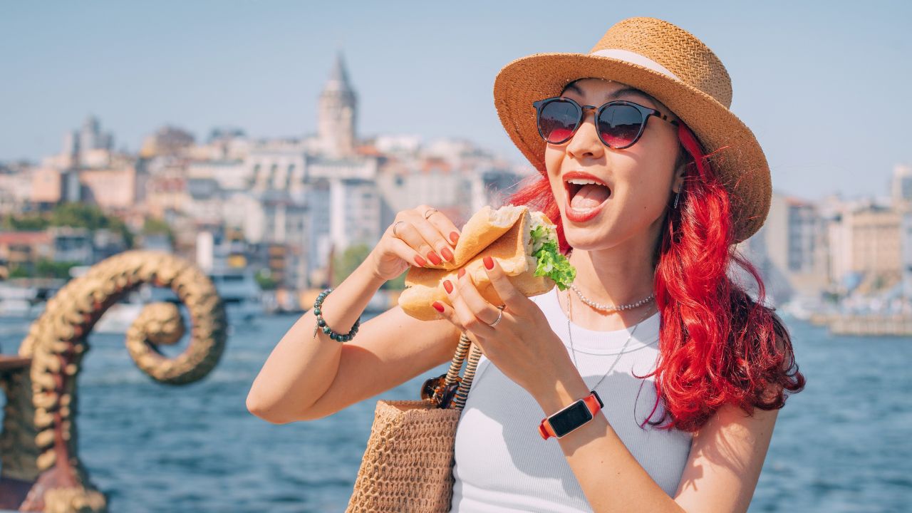A female tourist takes a bite of her fish sandwich, experiencing the vibrant street food culture of Istanbul during summer vacation.