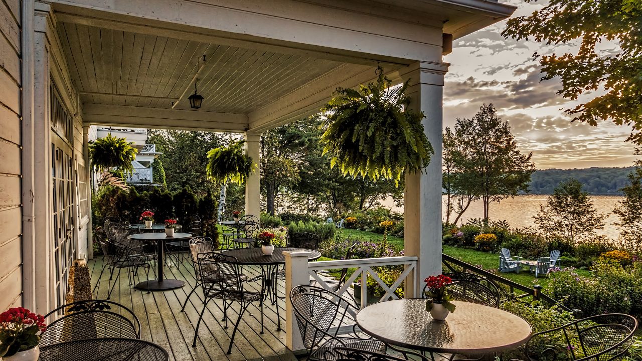 North Hatley, PQ, Quebec, Canada - September 5, 2014 : The balconey of a historic Quebec inn with bistro tables overlooks a lush perrenial garden beside Lake Missiwappi on an early summer morning.