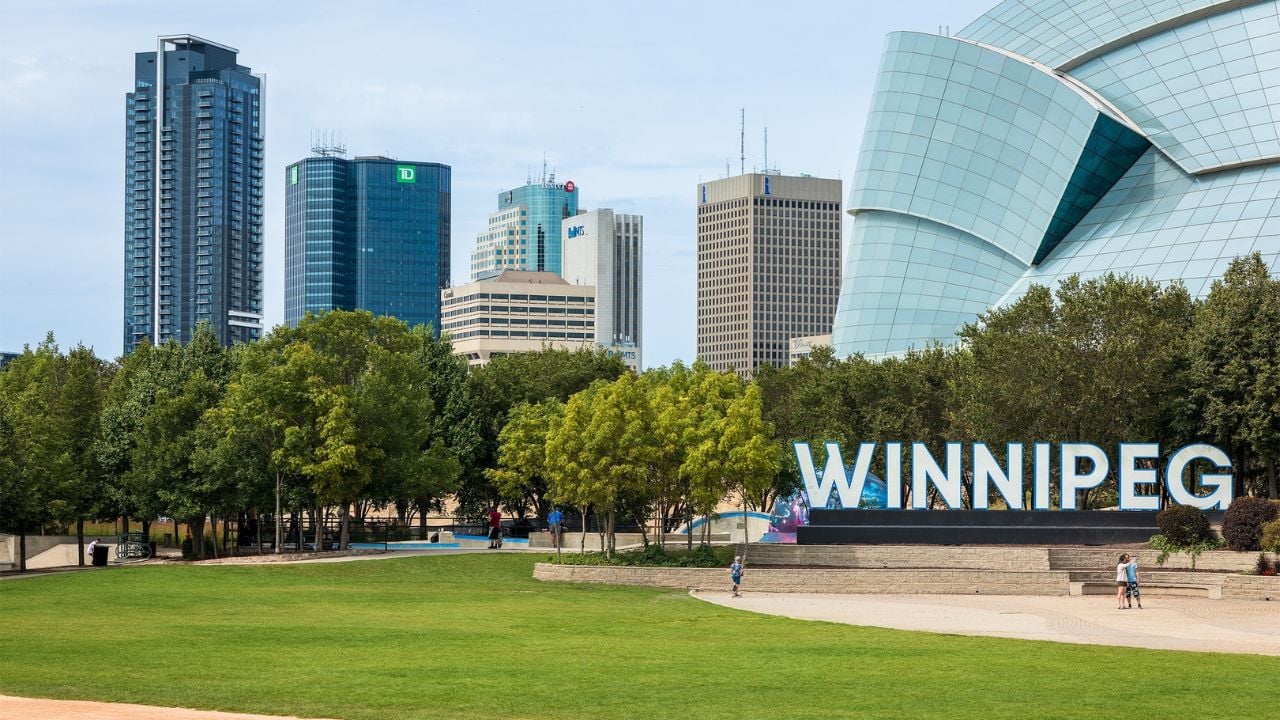 Winnipeg, Manitoba, Canada - August 26, 2024: The Winnipeg sign at the Forks with a view of downtown buildings in the background. A partial view of the Canadian Museum of Human Rights is on the right.