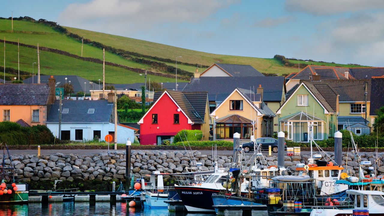 DINGLE, IE - Sep 15, 2021: A beautiful shot of boats parked on a pier with the background of the colorful town of Dingle, Ireland