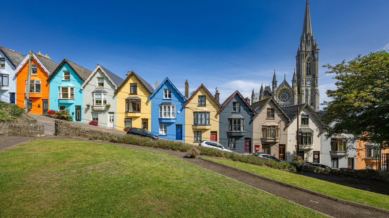 COBH, IRELAND - August 8th 2025: Colorful "deck of cards houses" on a steep street with a cathedral in the background