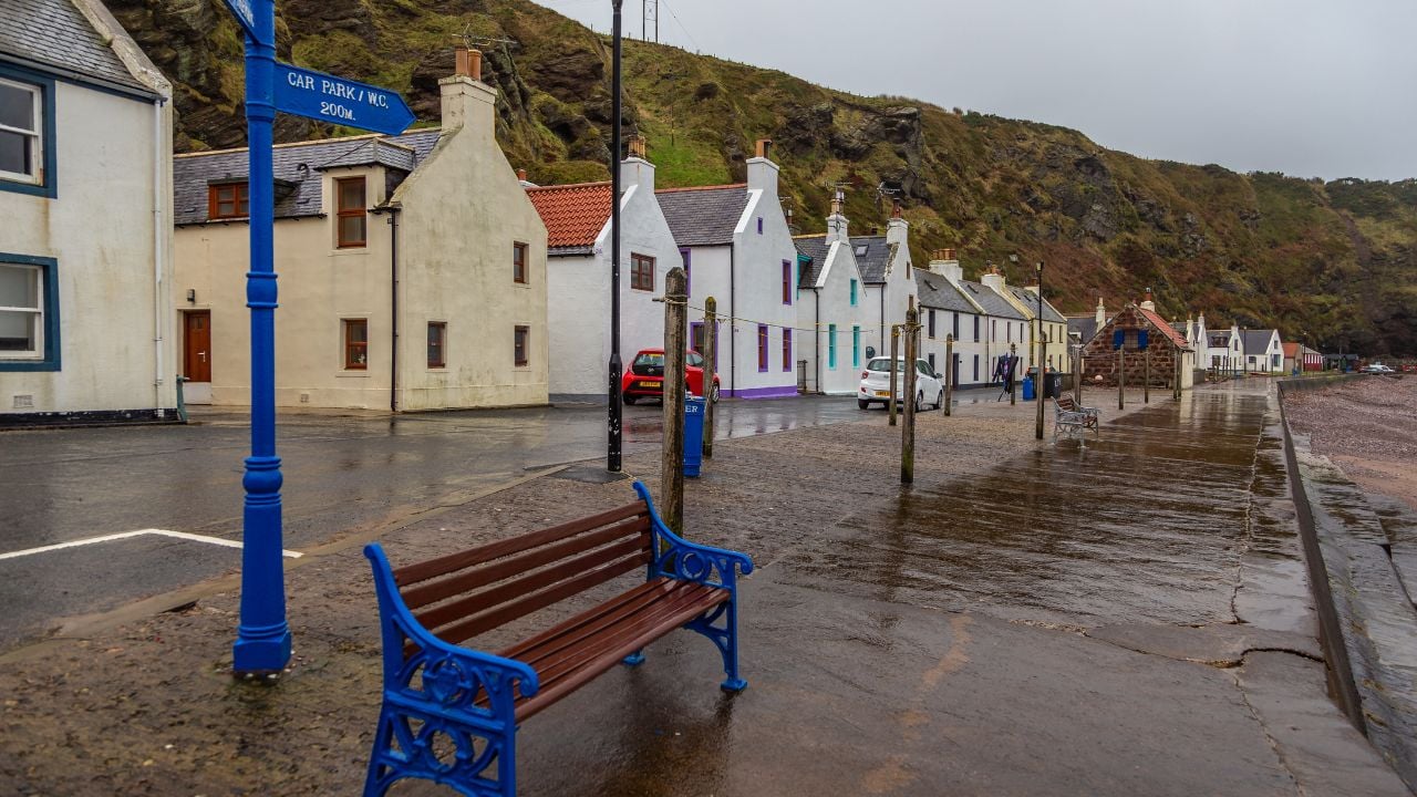 Pennan, Aberdeenshire, Scotland, UK - 05 February 2016: Quayside benches overlooking the North Sea. Historic houses in the background. Rainy day.
