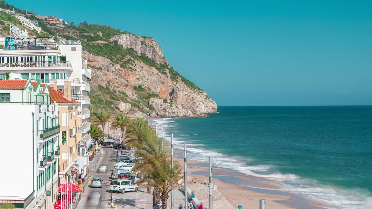 Aerial view on the coastal town of Sesimbra with palms on the street and beach in Portugal timelapse with blue sky and ocean