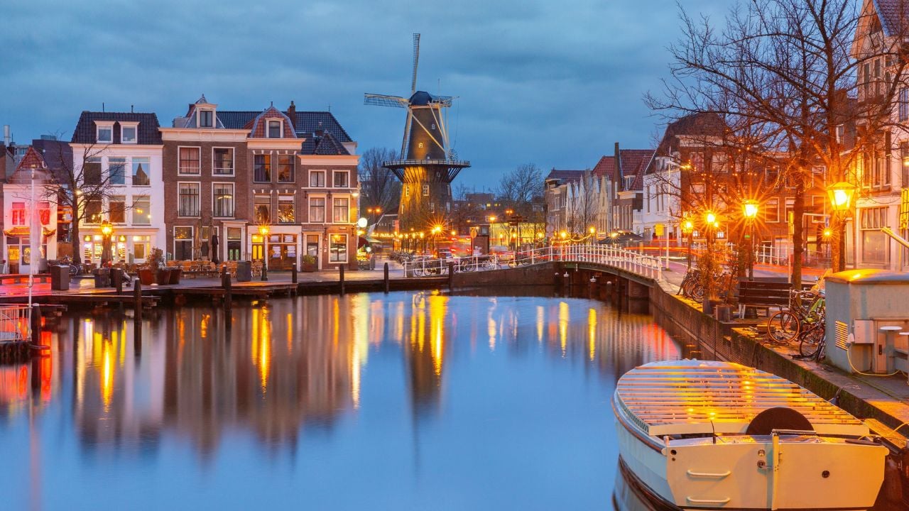 Traditional windmill and illuminated canal houses reflected in water in Leiden Netherlands