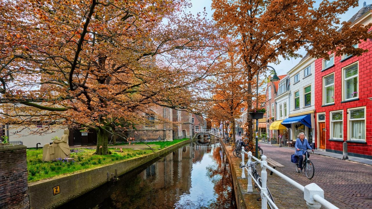 Delft, Netherlands - May 12, 2017: Delft street with canal and old houses with unidentified woman riding bicycle