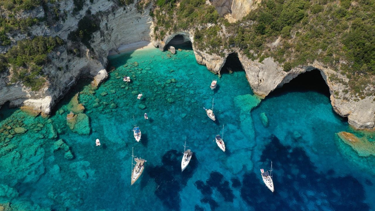 Aerial drone photo of paradise bay an caves of blue lagoon in beautiful island of Paxos visited by yachts and sail boats, Ionian, Greece