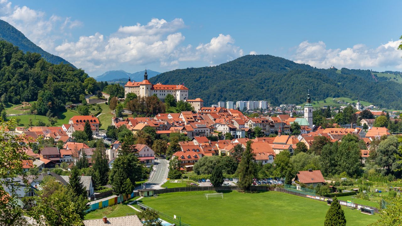 Škofja Loka, Slovenia - August, 2021: A panorama picture of Škofja Loka and its landmarks, such as the castle and the St. Jacob Church, cradled by the surrounding landscape, seen from afar.