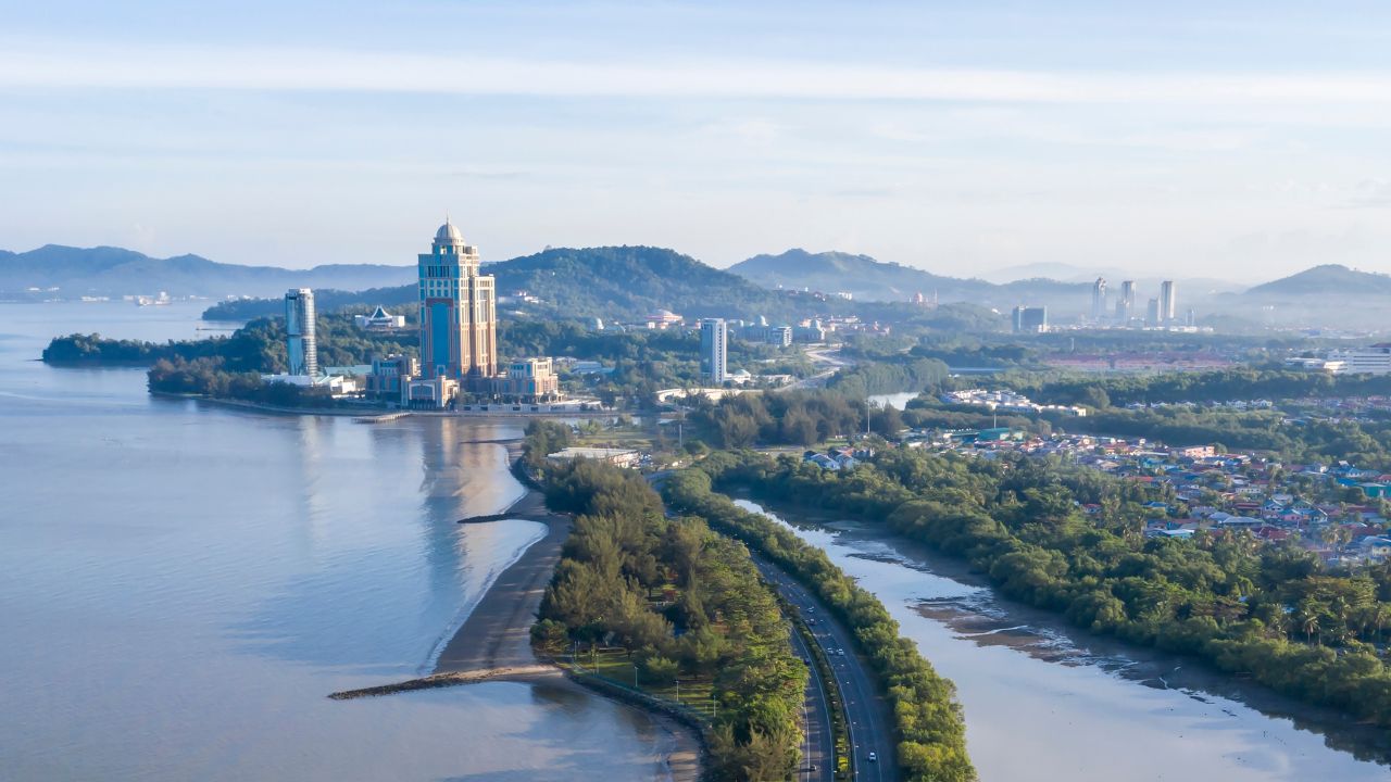 Aerial view of Kota Kinabalu cityscape with coastal buildings, lush greenery, and mountain backdrop in Sabah, Malaysia.