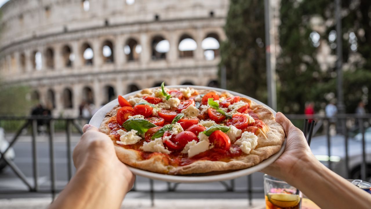 Colosseum (Colosseo) exterior with Margherita pizza in hand . Rome, Italy.