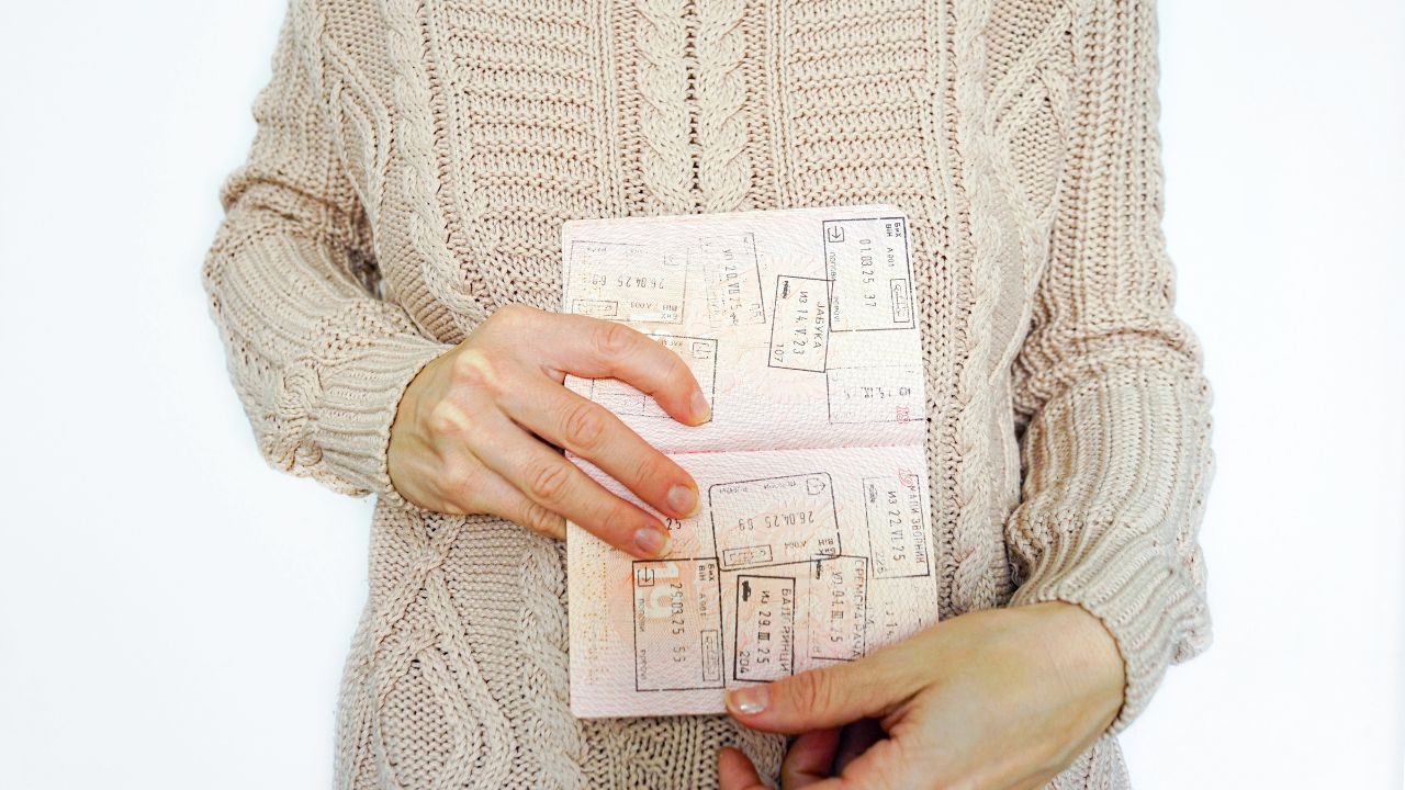 Hands displaying opened passport pages with numerous immigration stamps against a neutral background. Represents frequent traveler status, cross-border movement, and nomadic lifestyle validation.