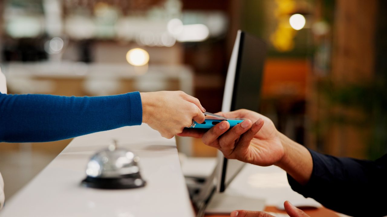 Hands, credit card and payment with machine at hotel, concierge or booking with hospitality service. People, receptionist and transaction at help desk with fintech, mobile app or reservation at lodge