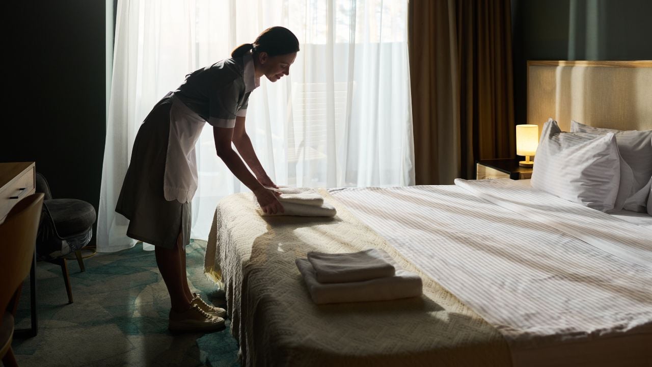Room attendant tidying a hotel room bed