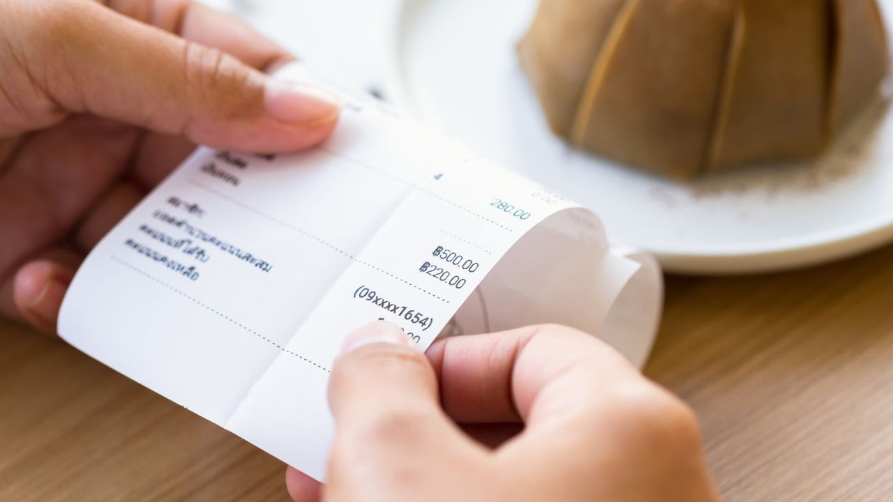 Closeup hand holding food bill to check the price with cake on background