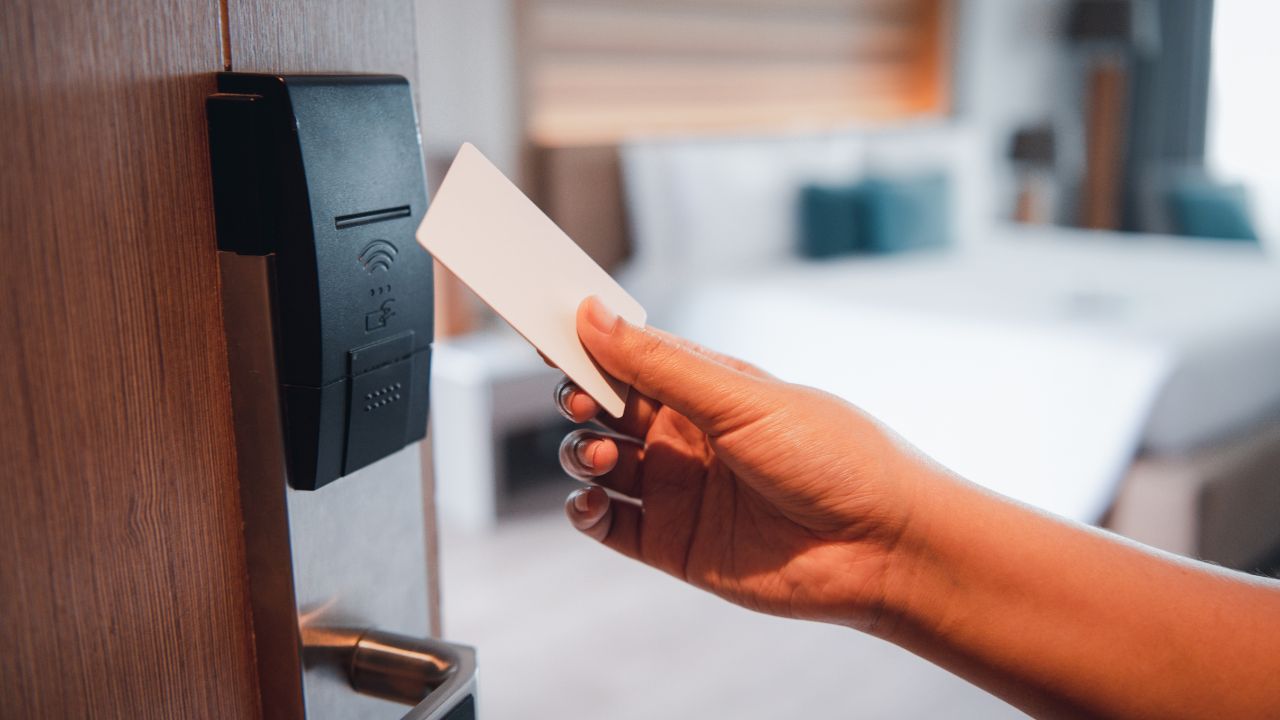 Hand holding key card to access the hotel room with bedroom background. Security and privacy concept.