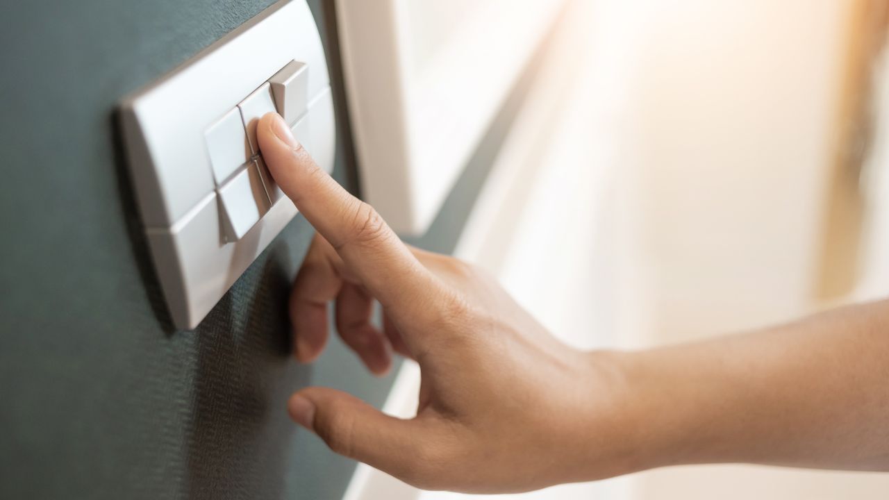 Close up of Female finger is turning on or off on light switch over green wall covering. Copy space.
