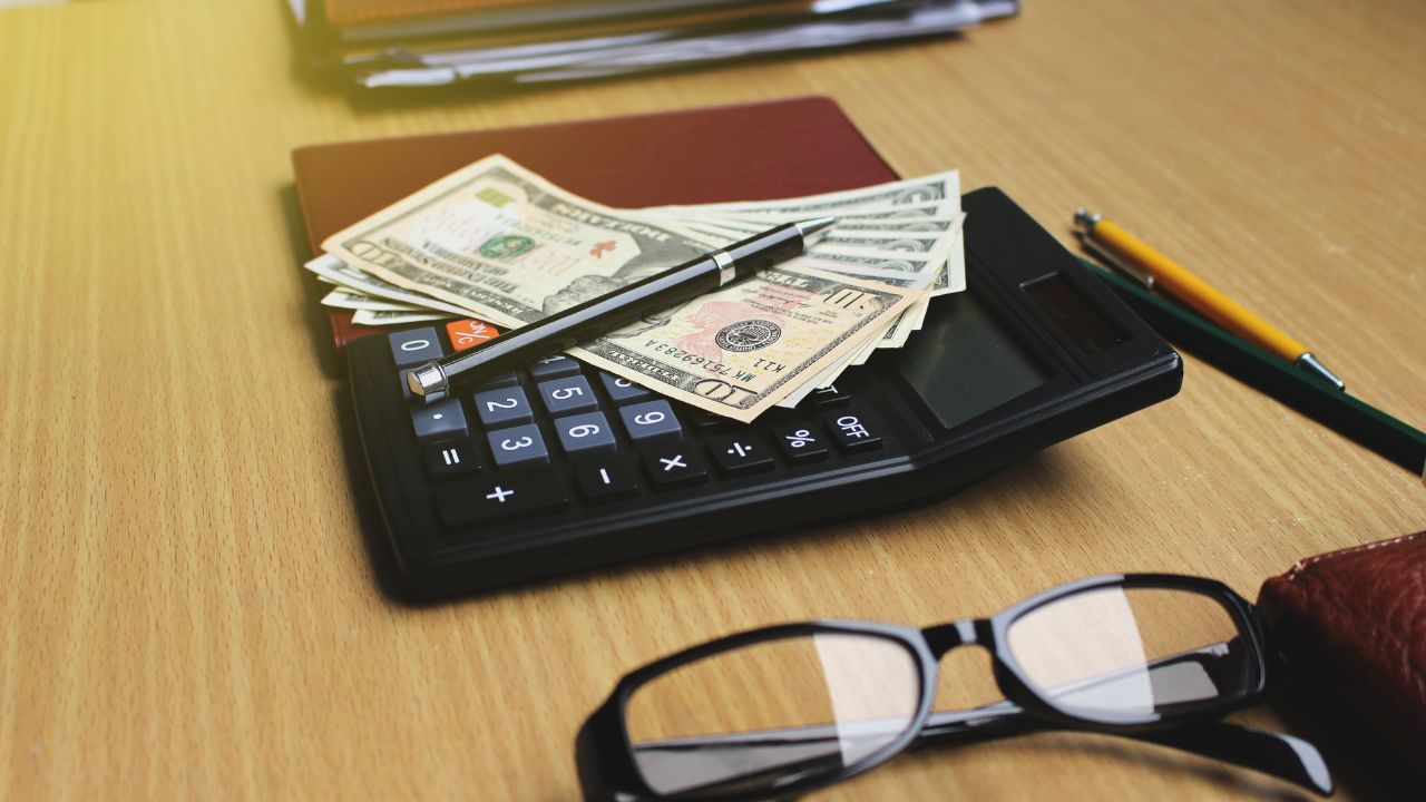 Office desk with US Dollars, smartphone with black screen, pen, calculator, wallet, and supplies with copy space.