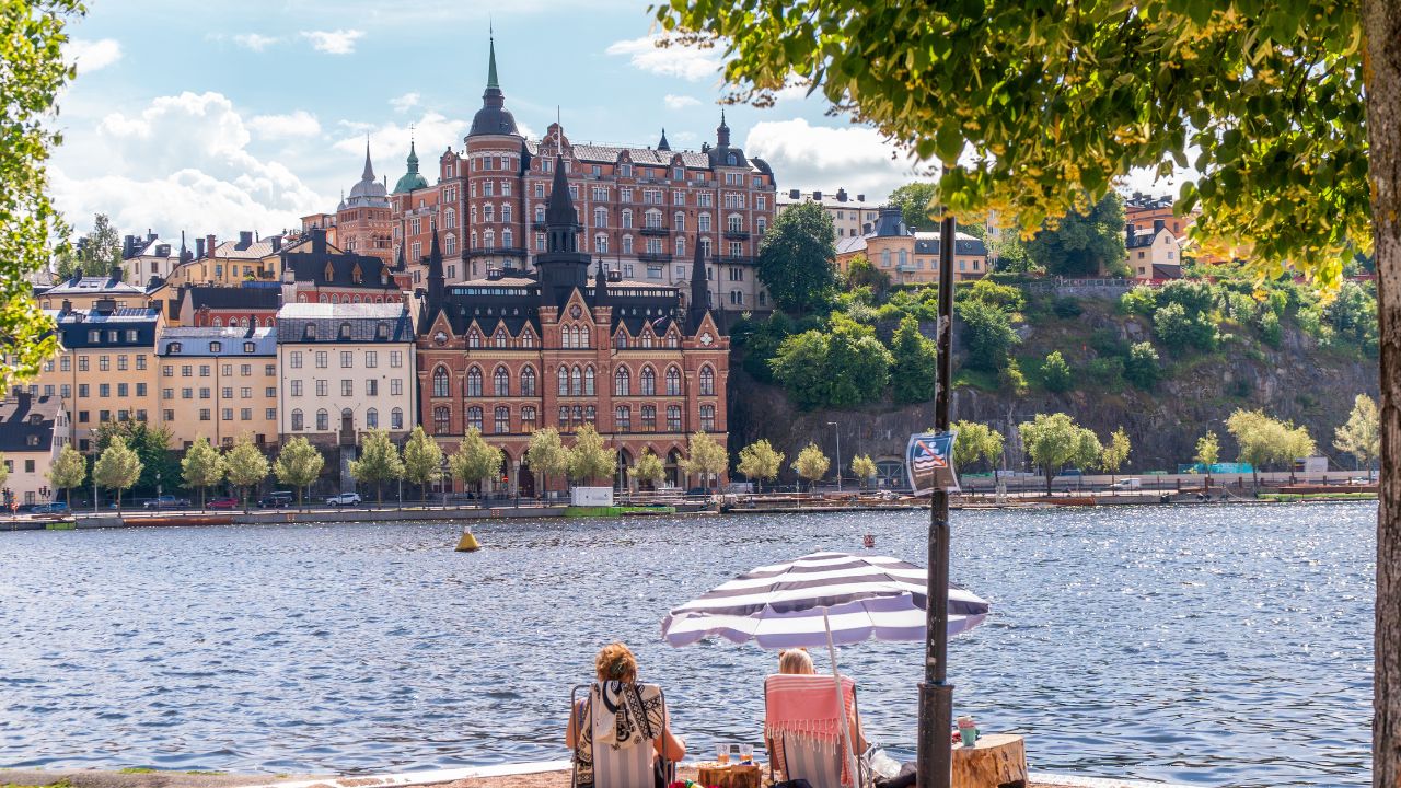 People enjoying the summer sun on a sand bed infront of historical buildings of Södermalm, from the island of Riddarholmen, near Lake Mälaren. Stockholm, Sweden
