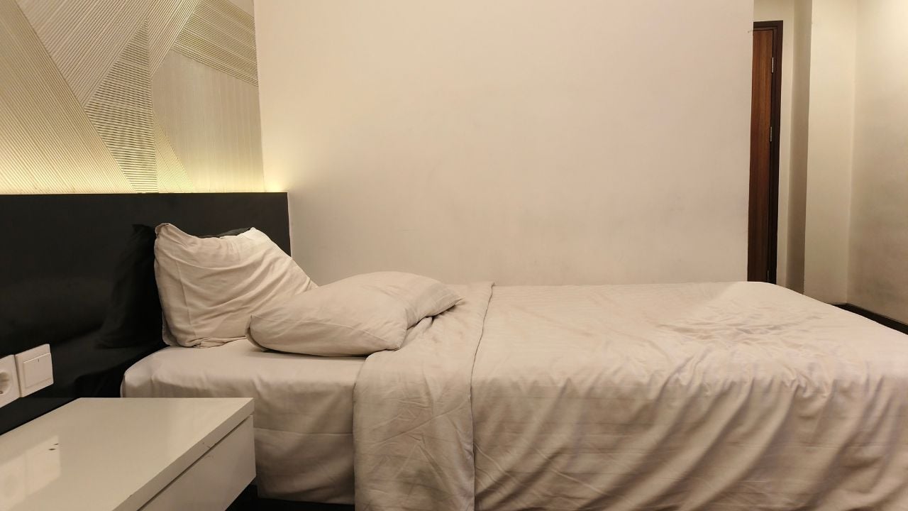 Cozy minimalist hotel room with a single bed, soft lighting, modern wall texture, and clean white linens. Comfortable space perfect for travel, relaxation, and accommodation themes.