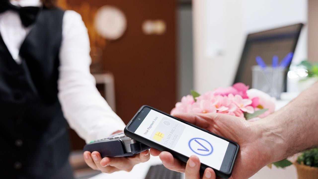 Detailed view of concierge helping elderly toruist with payment using smartphone and NFC technology. Close-up shot of male traveler paying using mobile device with assistance of hotel receptionist.