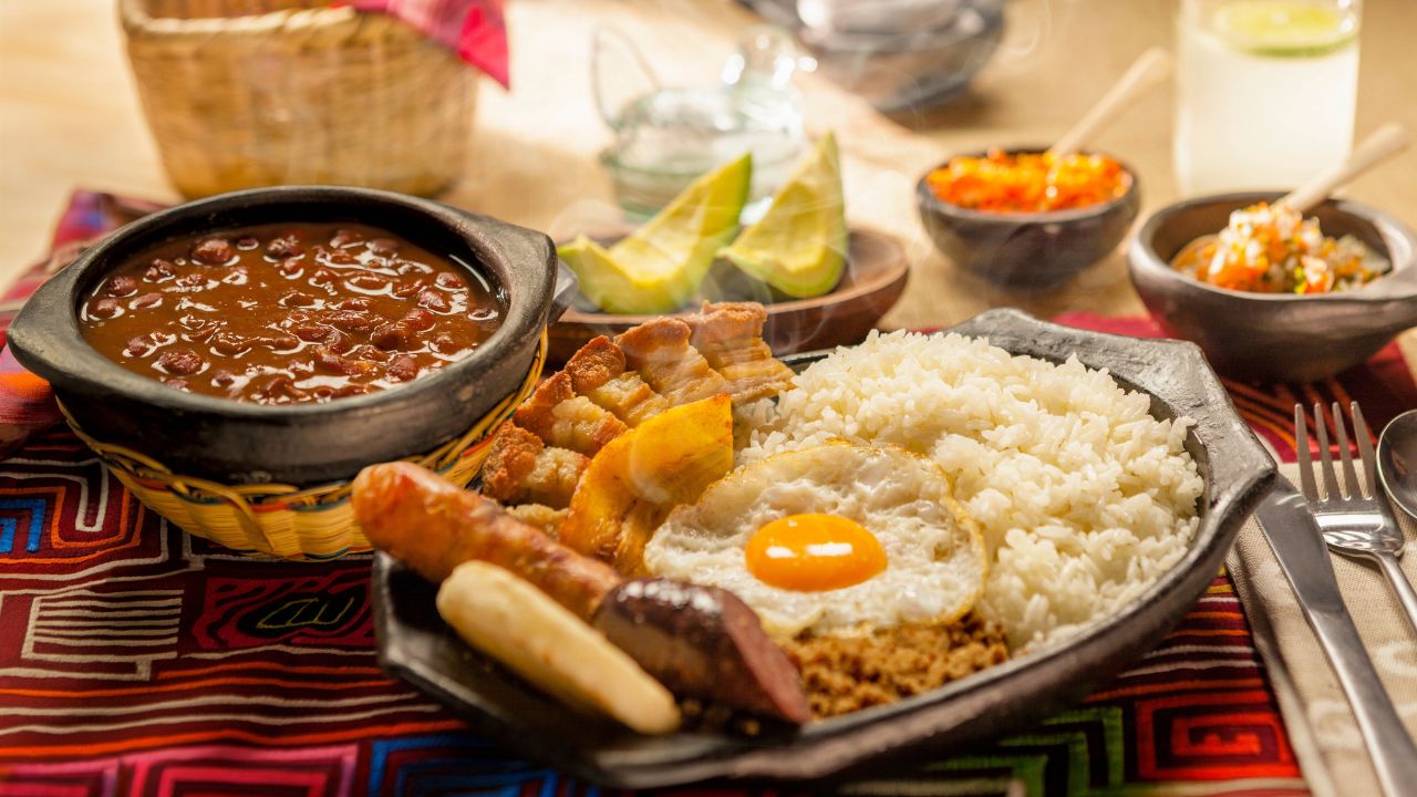 Traditional Colombian dish Bandeja Paisa with fried egg, beans, rice, chorizo, and pork rind served on a rustic table setting.