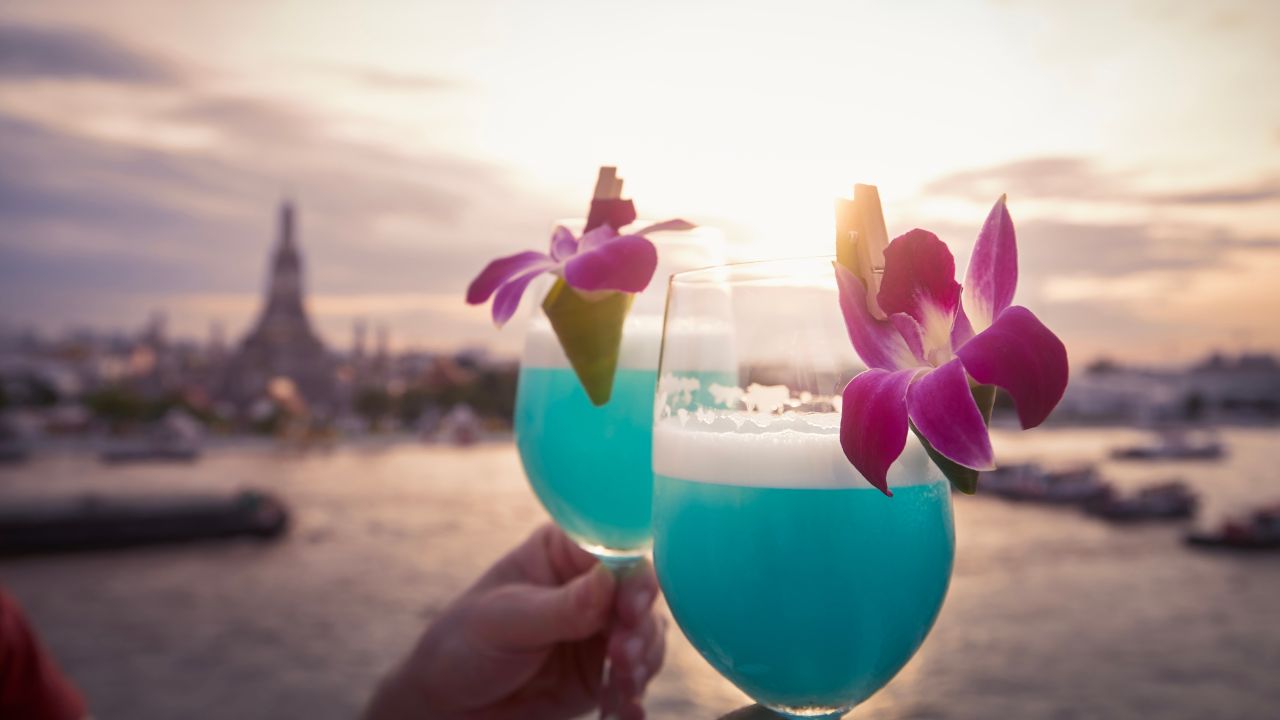 Cocktail drinks with blue curacao. Couple holding decorated drinking glasses against city view at sunset. Bangkok, Thailand