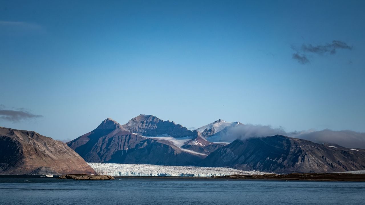 A stunning view of Arctic mountains and glacier under a clear blue sky in Svalbard, Norway, showcasing natural beauty and tranquility.
