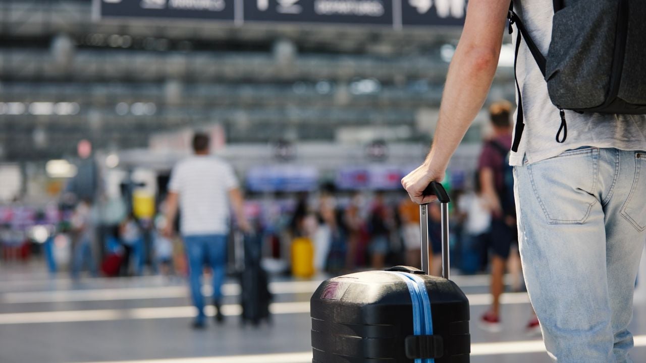 Traveling by airplane. Selective focus on hand of man holding suitcase. Traveler walking with luggage through airport terminal towards check-in. Suitcase