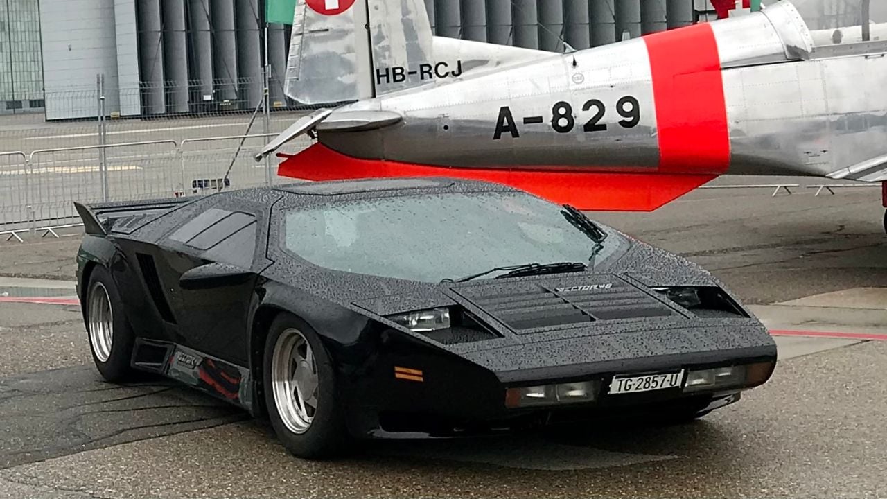 Black Vector W8 Front 3/4 view parked in an airport runway next to plane