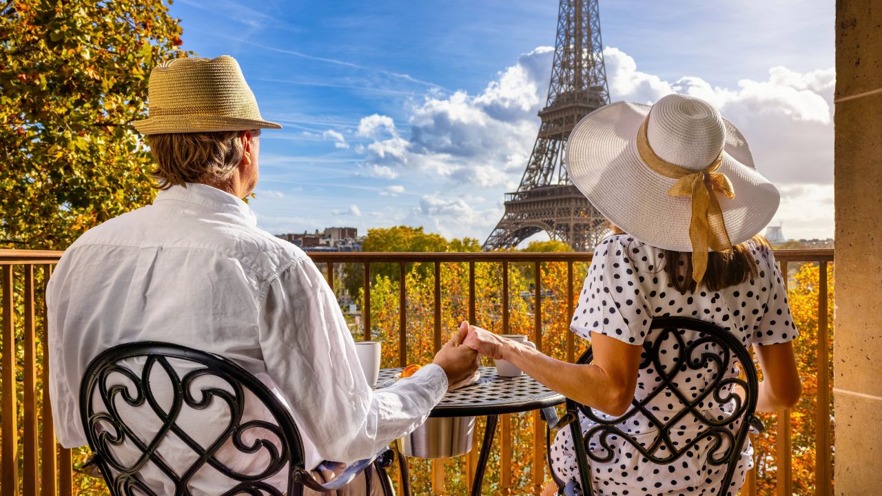 Rear view of a romantic couple holding hands on a balcony and enjoying the view to the Eiffel Tower in Paris, France