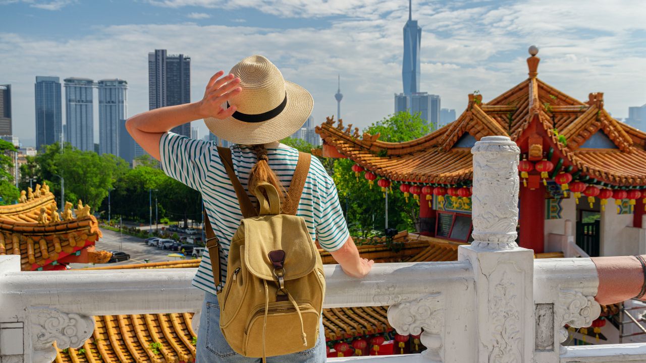 Female tourist in hat with backpack is enjoying view of Kuala Lumpur from the Thean Hou Temple, Malaysia. Merdeka 118 is visible in background. Kuala Lumpur is a popular tourist destination of Asia.