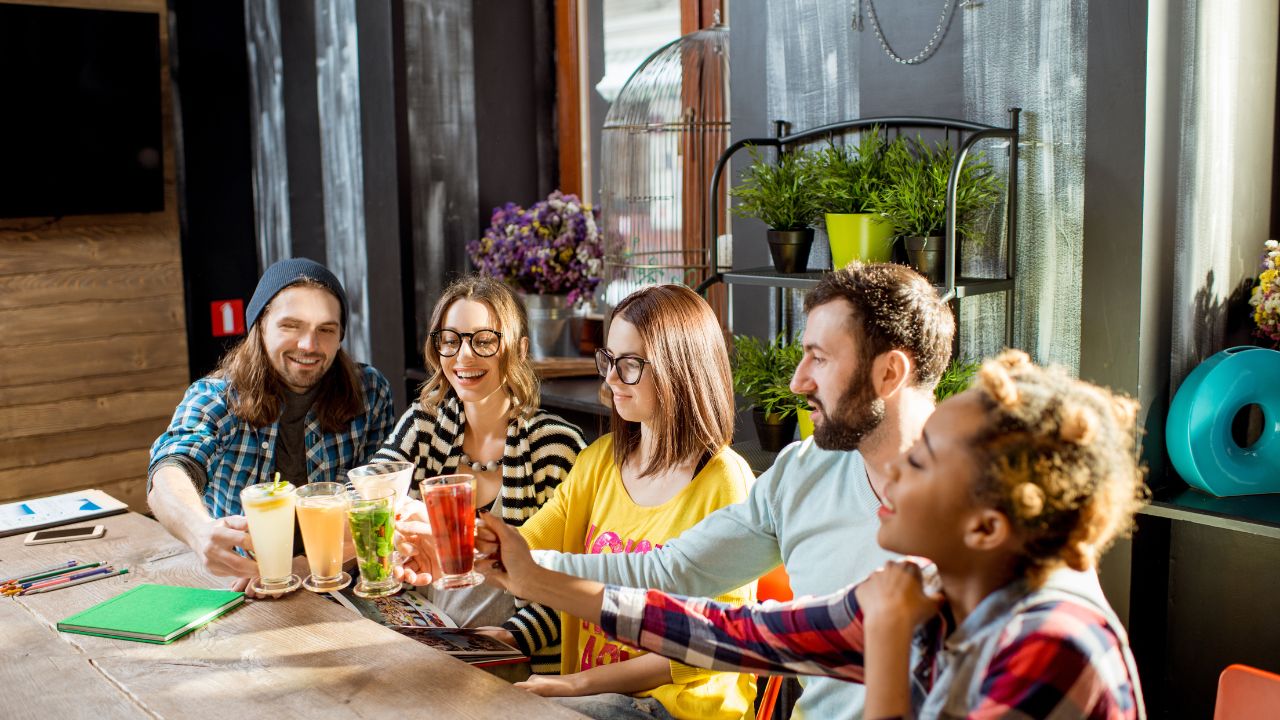 Multi ethnic group of friends having fun clinking glasses with tasty hot drinks sitting in the modern cafe interior