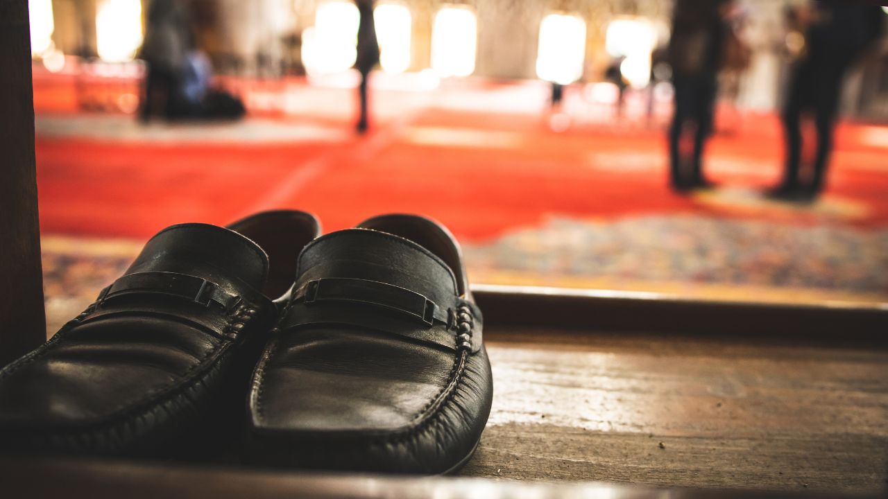 Black shoes on the shelf in a mosque with muslim people walking and praying on the background. Footwear during the pray. Traditions and etiquete in muslim countries.