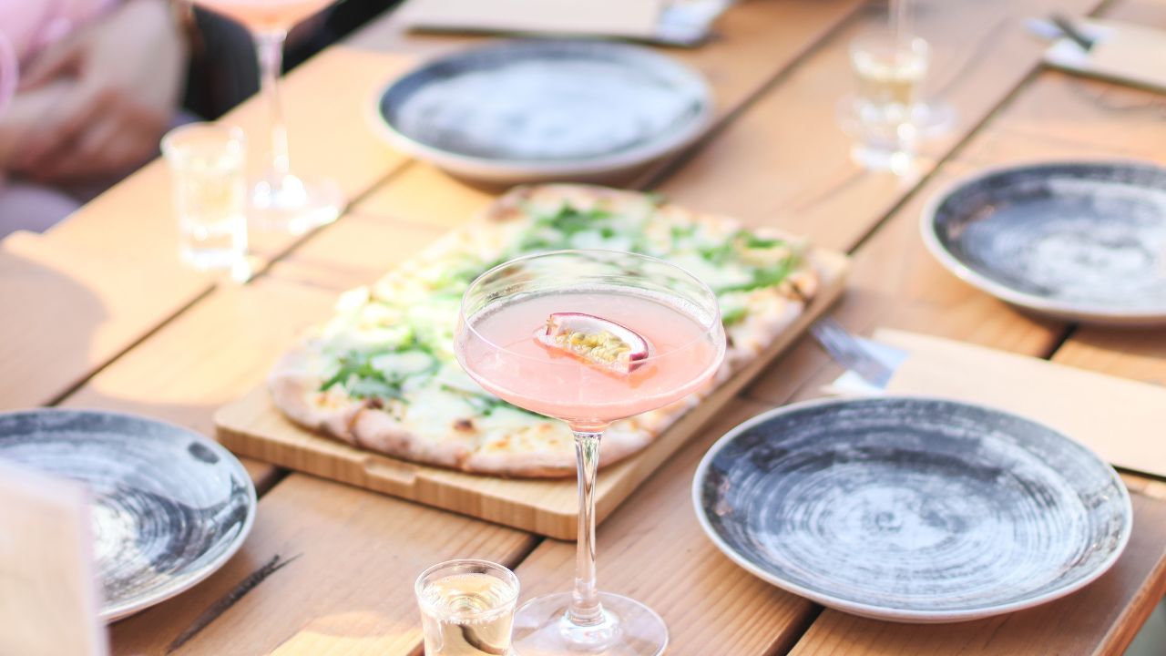 Alcoholic drink with passion fruit in a beautiful glass with a glass of vodka on a wooden table with pizza and empty gray plates in a floating restaurant on a clear sunny spring day,Concept of table s