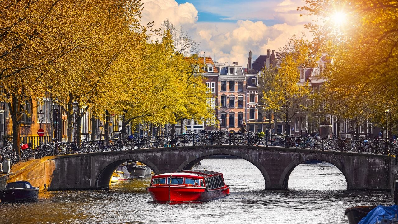 Channel in Amsterdam Netherlands Holland houses under river Amstel. Pleasure boat under the bridge. Landmark old european city spring landscape with sunshine.