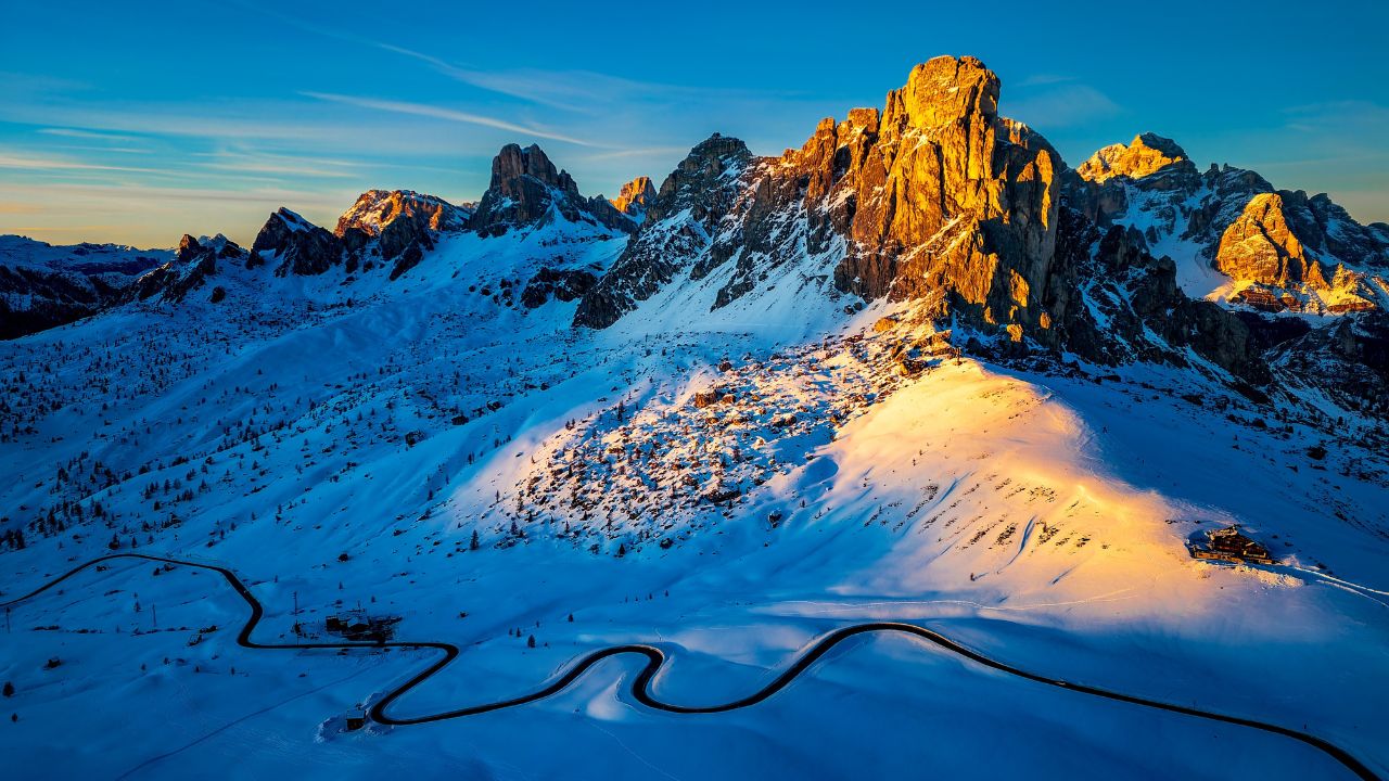 The Passo Giau mountain pass in the Italian Dolomites in winter. Snow-covered Passo Giau at sunset. A mountain illuminated by the golden sun. Winter composition.