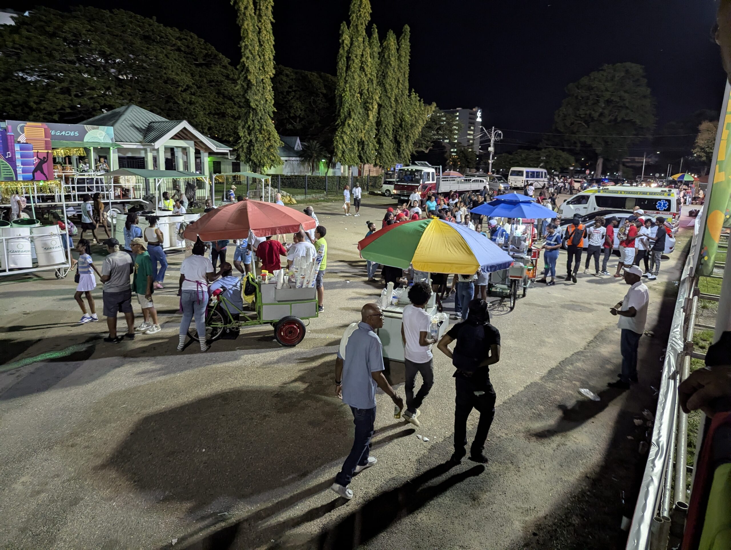 Port of Spain, Trinidad and Tobago - January 18, 2026 - People purchasing food and drinks from vendors on vending carts with colorful umbrellas at a Carnival 2026 event at the Queen's Park Savannah.