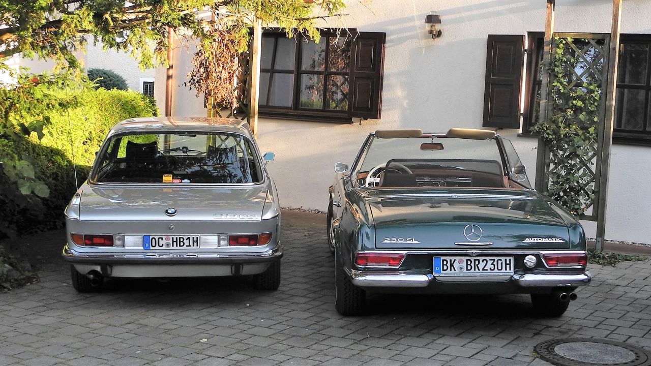 Rear view of a vintage BMW 3.0 CS and a Mercedes-Benz 230 SL "Pagoda" convertible parked together