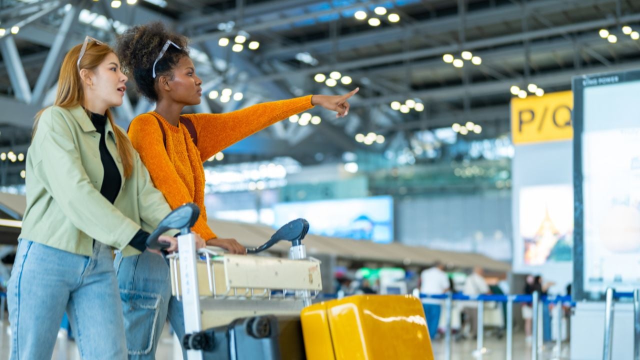 Happy woman friend holding passport and suitcase walking together to airline check in counter in airport terminal. Attractive girl enjoy and fun travel on holiday vacation with airplane transportation