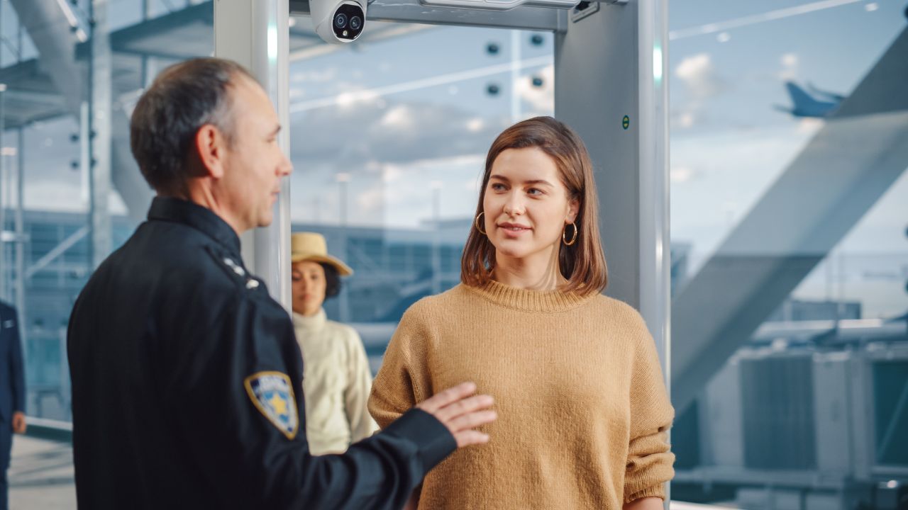 Airport Terminal: Security Officer Checks and Separates Diverse Group of People Walking Through Metal Detector Scanner Gates for Plane Flight Boarding. Crowd of Travelers Going on Vacation Trips