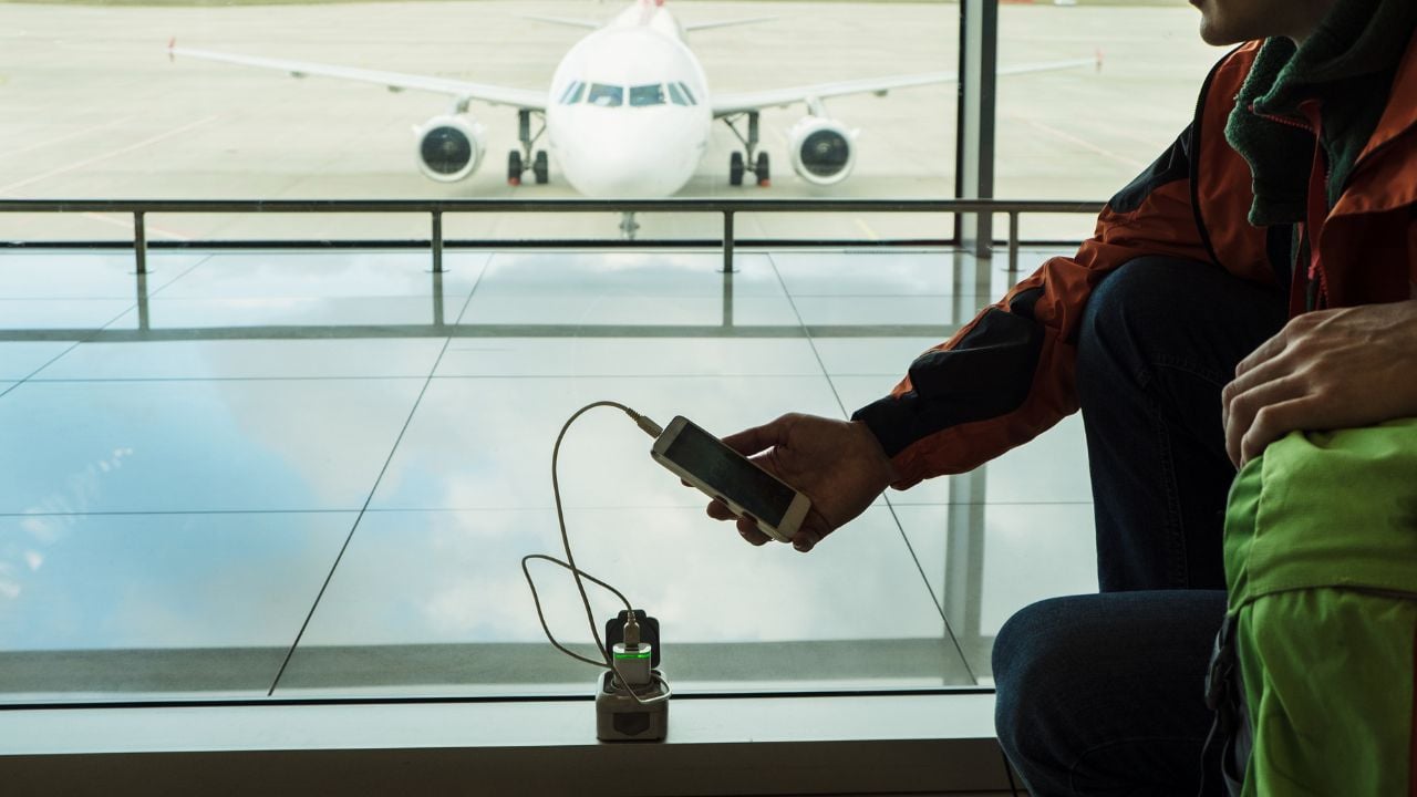 Travel by airplane. Passenger charging mobile device at the lounge of airport terminal. Silhouette of a man with phone and wire.