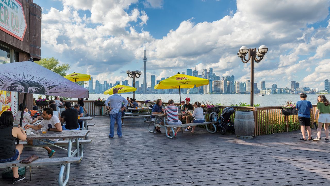 TORONTO, CANADA - JUNE 30, 2019: Toronto City view from restaurant in Central island on June 30, 2019 in Toronto, Canada. People relax in a beach restaurant on Ontario lake and view of Toronto city.