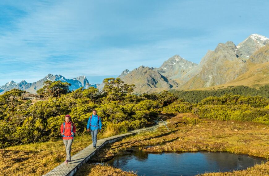 New Zealand Hiking. Young hiking couple walking on trail at Routeburn Track during sunny day. Hikers are carrying backpacks while tramping Key Summit Track in Fiordland National Park in New Zealand.